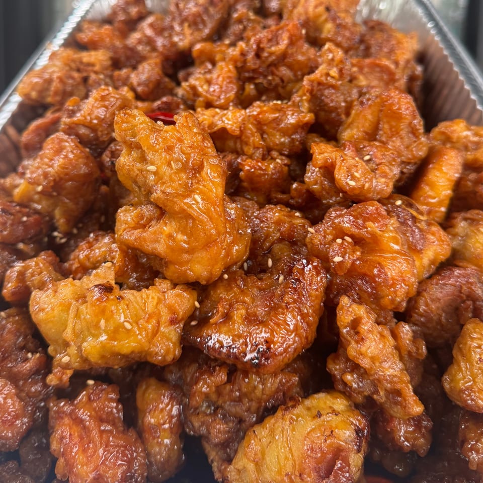 Close-up of Volcano Island's Korean fried chicken, coated in a glossy, reddish-brown sauce with sesame seeds.