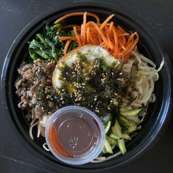 Bibimbap in a black bowl with beef, vegetables, fried egg, and a side of sauce.