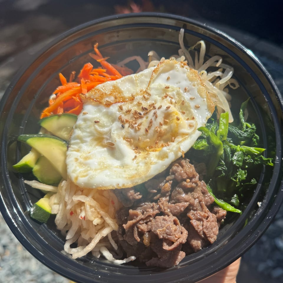 Close-up of a Korean bibimbap bowl with beef, fried egg, carrots, zucchini, and spinach.