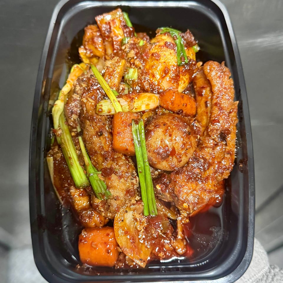 Korean braised short ribs (galbi jjim) with carrots, potatoes, and green onions in a black container.