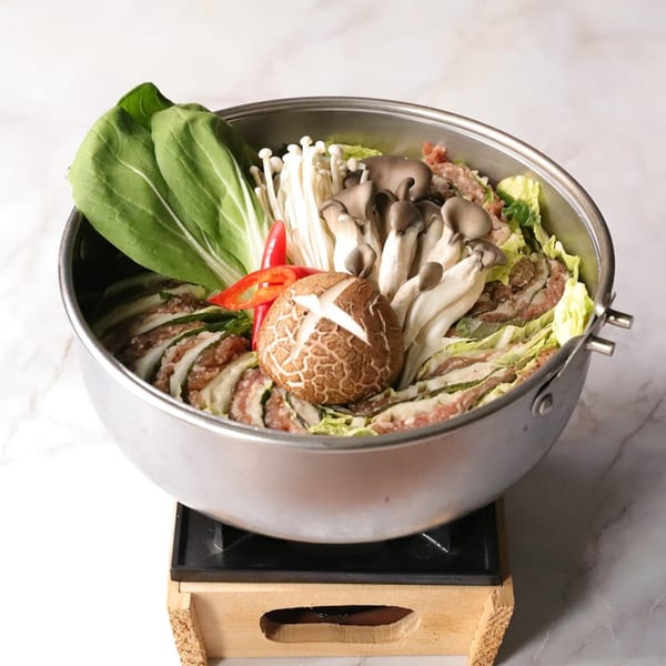Korean hot pot with mushrooms, bok choy, and sliced meat in a metal pot on a wooden stand.